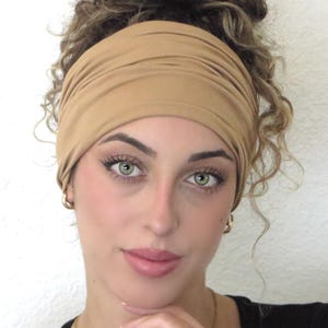 May include: A tan stretchy headband worn on a person with curly hair. The headband is made of a soft, comfortable fabric and is designed to be worn comfortably all day long.