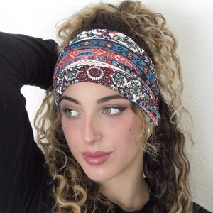 May include: A woman with curly hair is wearing a wide headband with a colorful paisley pattern. The headband is made of fabric and has a blue, red, and white color scheme.