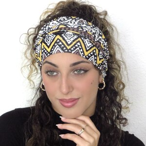 May include: A woman with curly brown hair is wearing a black and white headband with a yellow and brown geometric pattern. The headband is tied in a knot at the top of her head.