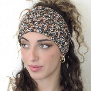 May include: A woman with curly brown hair is wearing a black and brown floral headband. The headband is made of a soft, stretchy fabric and has a subtle sheen.
