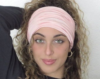 May include: A pink stretchy headband worn by a person with curly hair. The headband is made of a soft, comfortable fabric.