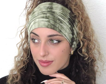 May include: A green and white tie-dye headband made from a soft, stretchy fabric. The headband is being worn by a person with long, curly hair.