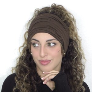 Pode incluir: Uma faixa de cabeça elástica marrom usada por uma pessoa com cabelo encaracolado. A faixa de cabeça é feita de um tecido macio e confortável e é projetada para ser usada em torno da cabeça.