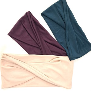 May include: Three fabric headbands in different colors: beige, burgundy, and teal. The headbands are twisted and folded, creating a unique and stylish look.