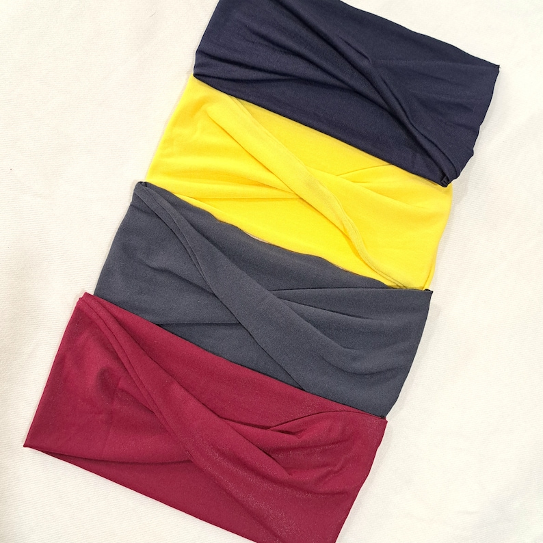 May include: Four fabric headbands in different colors: burgundy, dark gray, yellow, and navy blue. The headbands are folded and stacked on top of each other.