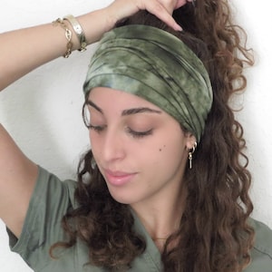 Puede incluir: Una diadema verde te&ntilde;ida con tinte anudado se lleva en la cabeza. La diadema ancha es de tela suave. La persona lleva una camisa verde y joyas de oro, incluyendo pendientes, un collar y pulseras.