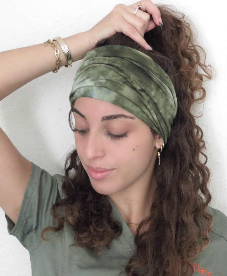 Puede incluir: Una diadema verde te&ntilde;ida con tinte anudado se lleva en la cabeza. La diadema ancha es de tela suave. La persona lleva una camisa verde y joyas de oro, incluyendo pendientes, un collar y pulseras.