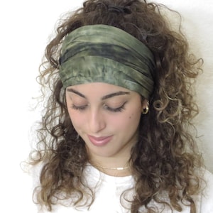 Puede incluir: Una diadema ancha de color verde oliva con detalles en verde oscuro se lleva en la frente. La tela parece suave y ligeramente texturizada. La diadema se coloca sobre un fondo de cabello casta&ntilde;o rizado y un fondo blanco.