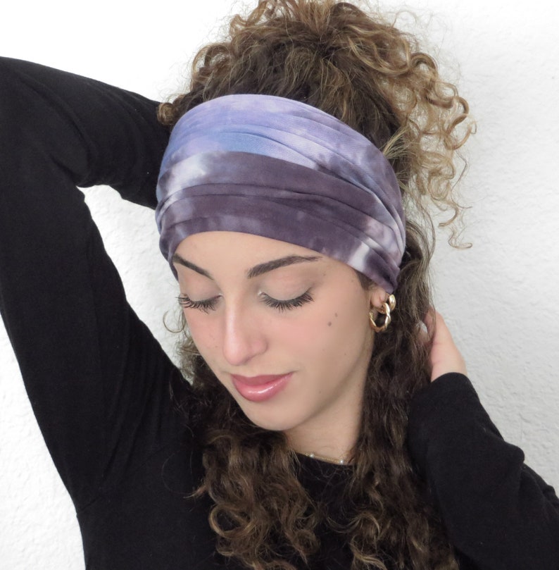 May include: A woman with curly brown hair is wearing a purple and blue tie-dye headband. The headband is made of soft, stretchy fabric and is perfect for adding a touch of color to any outfit.