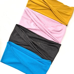 May include: Four fabric headbands in different colors: turquoise, gray, pink, and mustard yellow. The headbands are folded and stacked on top of each other.