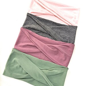 May include: Four fabric headbands in different colors: green, pink, mauve, and gray. The headbands are folded and stacked on top of each other.