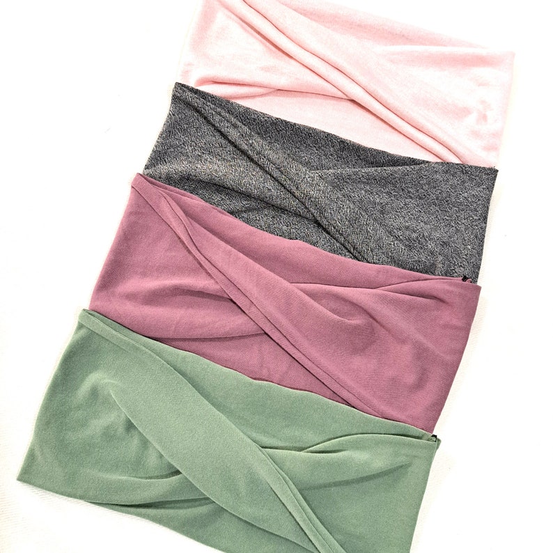 May include: Four fabric headbands in different colors: green, pink, mauve, and gray. The headbands are folded and stacked on top of each other.