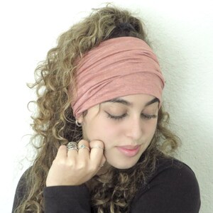 May include: A woman with curly hair is wearing a dusty rose colored headband. The headband is made of a soft, stretchy fabric.