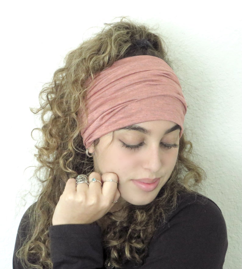 May include: A woman with curly hair is wearing a dusty rose colored headband. The headband is made of a soft, stretchy fabric.