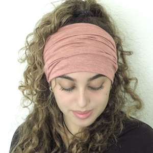 May include: A woman with curly hair is wearing a pink stretchy headband. The headband is made of a soft, comfortable fabric and is perfect for keeping hair out of the face.