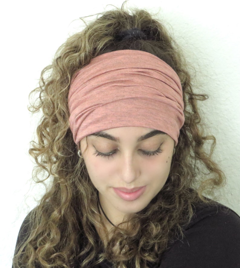 May include: A woman with curly hair is wearing a pink stretchy headband. The headband is made of a soft, comfortable fabric and is perfect for keeping hair out of the face.