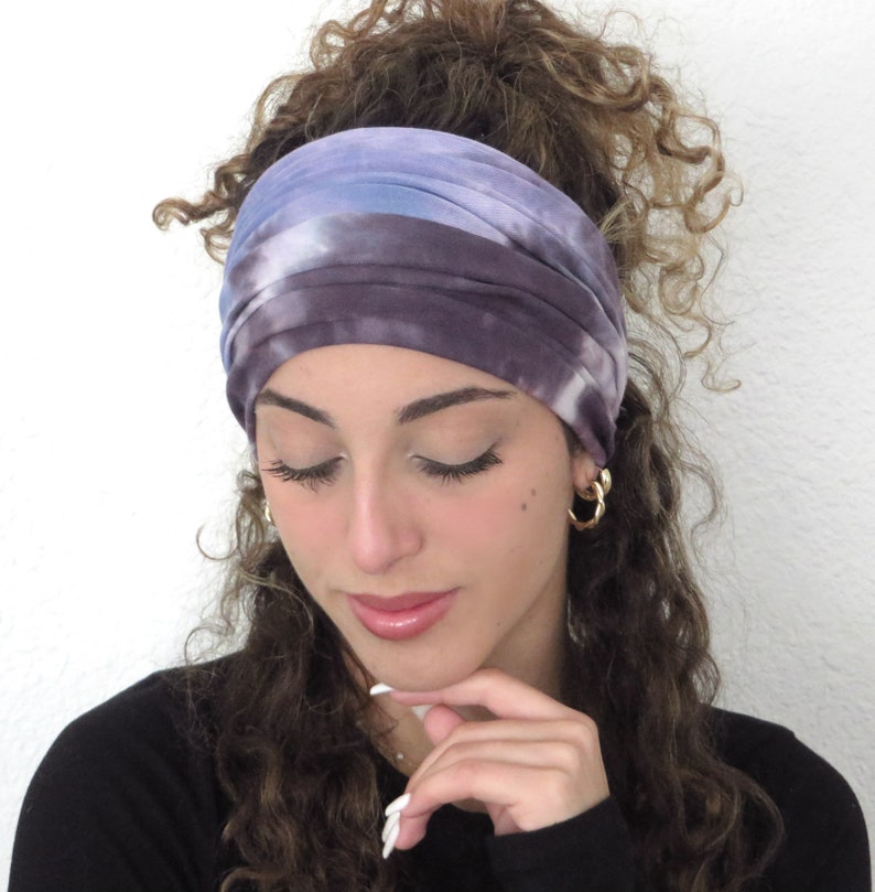 May include: A purple and blue tie-dye headband with a white background. The headband is worn by a person with curly brown hair.