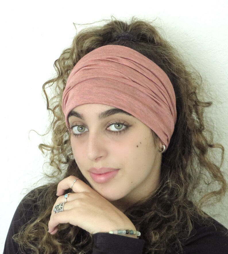 May include: A woman with curly brown hair is wearing a pink stretchy headband. The headband is folded over several times and is worn around her forehead.