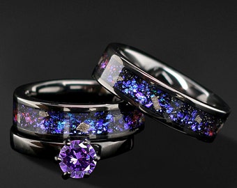Può includere: Due anelli neri con una finitura iridescente viola e blu. L'anello superiore ha una grande pietra preziosa viola al centro.