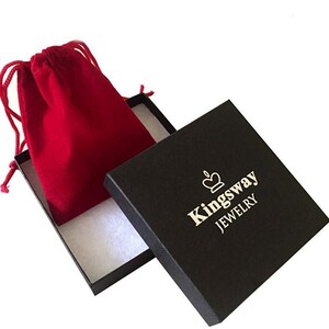 Peut inclure: Une bo&icirc;te &agrave; bijoux carr&eacute;e noire avec un int&eacute;rieur blanc et un logo couronne dor&eacute; au-dessus du texte Kingsway JEWELRY. Une pochette &agrave; cordon en velours rouge est plac&eacute;e dans la bo&icirc;te ouverte, avec des cordons rouges assortis et une texture douce.