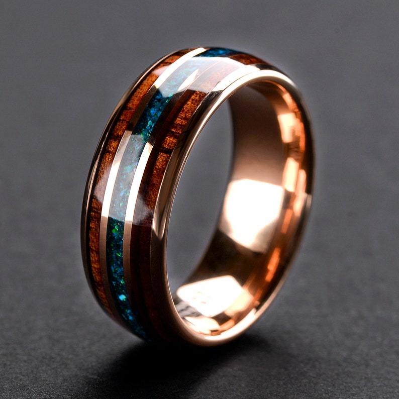 May include: A rose gold tungsten carbide ring with a brown wood inlay and a blue and green opal inlay.