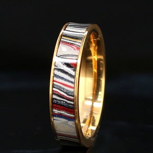May include: A gold band ring with a colourful, striped inlay. The inlay features a variety of colours, including black, white, red, and blue.