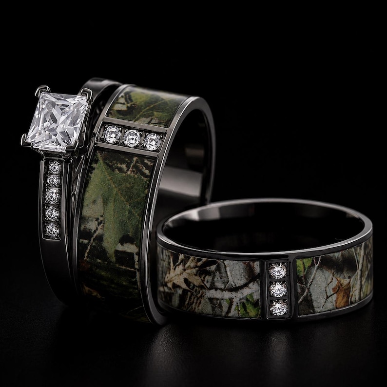 Peut inclure: Un ensemble de deux bagues en m&eacute;tal noir avec une incrustation &agrave; motif camouflage. La bague de fian&ccedil;ailles pr&eacute;sente une pierre claire taille princesse et de petites pierres rondes sur l'anneau. L'alliance assortie comporte trois petites pierres.