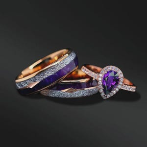 May include: A set of three rings featuring rose gold bands with a textured metallic inlay and a deep purple center. One ring includes a pear-shaped purple gemstone surrounded by a halo of small white stones set into a rose gold band.