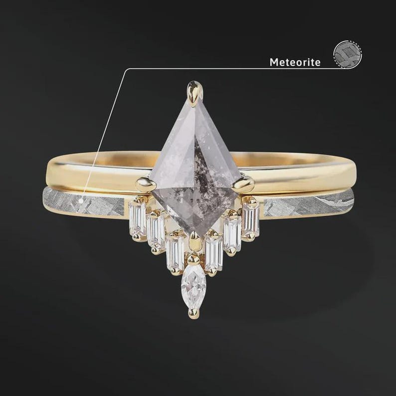 Pode incluir: Um conjunto de an&eacute;is de duas pe&ccedil;as com uma banda de ouro e uma banda de meteorito. O anel de noivado tem uma pedra grande, cinzenta, em forma de pipa com pedras menores de corte baguette e uma pedra em forma de marquesa. A palavra "Meteorite" est&aacute; na imagem.