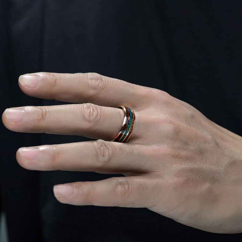 May include: A close-up of a hand wearing a ring with multiple bands of wood and turquoise inlay.