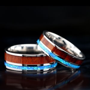 May include: Two wooden rings with a blue opal inlay. The rings are made of Koa wood and have a silver band.