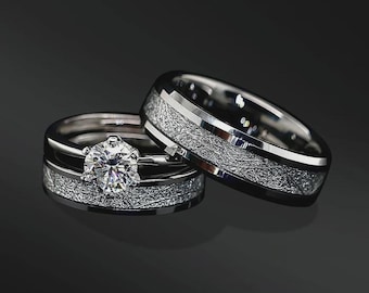 May include: Two silver-toned rings with a textured, cratered surface finish. One ring features a prominent, round, multi-faceted clear stone held in a six-prong setting, while the other is a wider band with a smooth, polished edge border.