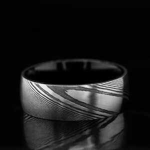 May include: A wide silver band with a unique, swirling pattern. The band is made of Damascus steel and has a polished finish.