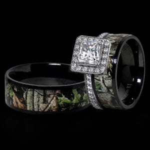 Puede incluir: Un conjunto de dos anillos con incrustaciones de patrón de camuflaje con motivos de hojas verdes, marrones y negras. Un anillo es una banda ancha y el otro tiene una piedra central cuadrada de corte princesa rodeada por un halo de piedras claras.