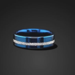 May include: A polished blue ring featuring a central horizontal band with a textured, silver-colored finish. The ring has a smooth, reflective surface on the top and bottom edges, creating a distinct contrast with the rough, metallic inlay.
