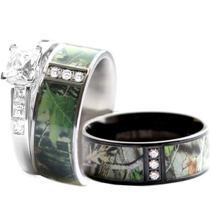 Peut inclure: Une bague de fian&ccedil;ailles argent&eacute;e avec une pierre centrale taille princesse et des pierres lat&eacute;rales serties, accompagn&eacute;e d'une alliance assortie avec une incrustation camouflage verte et trois petites pierres. Une seconde bague noire assortie.