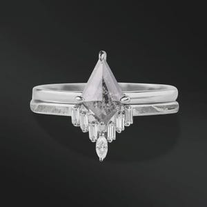 May include: A silver engagement ring set with a large, kite-shaped, gray diamond as the focal point. The ring is paired with a matching band. Smaller, rectangular and marquise-cut diamonds adorn the main ring, creating a unique, elegant design.