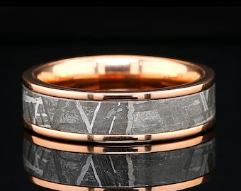 May include: A rose gold band with a meteorite inlay. The band is polished and has a smooth finish. The meteorite inlay is a dark gray color with a unique pattern of white lines.