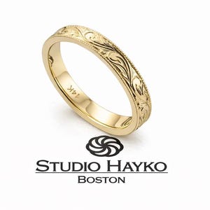 Pode incluir: Uma aliança de casamento em ouro 14K com um padrão floral gravado. O anel está sobre um fundo branco. O logotipo da marca "STUDIO HAYKO BOSTON" é visível abaixo.