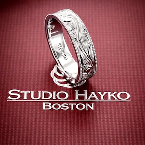 May include: A sterling silver ring with intricate floral engraving. The ring has a detailed pattern around the band and the word "STERLING" is engraved on the inside. The ring is displayed on a red surface with the text "STUDIO HAYKO BOSTON".