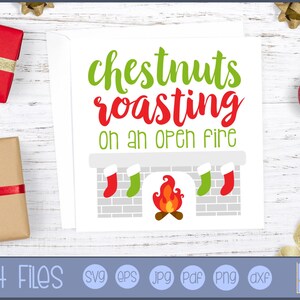 May include: A white card with the text "chestnuts roasting on an open fire" in green and red. The card features a fireplace graphic with stockings and a fire. Presents and ornaments are in the background. Cut files are listed below the card.
