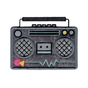 May include: An embroidered patch of a vintage boombox in grey and black, featuring a teal and grey cassette tape, a pink and yellow play button, and a teal sound wave.