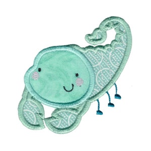 May include: A light blue embroidered scorpion with a smiling face. The scorpion has a patterned design on its body and tail.