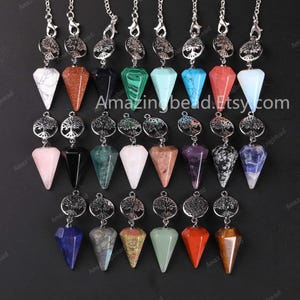 May include: Twenty assorted crystal point pendulums with silver tree of life charms. The crystals are in various colors, including pink, green, blue, red, and black.