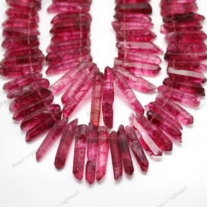 May include: A strand of pink quartz crystal beads, each bead is a long, thin, pointed shape. The beads are arranged in a loose, flowing pattern.