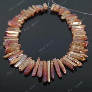 May include: A strand of orange and gold iridescent crystal point beads. The beads are faceted and have a pointed shape. The beads are strung on a clear thread.
