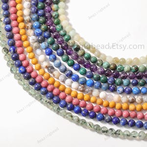 May include: A variety of gemstone beads in different colors, including green, blue, purple, pink, and yellow. The beads are strung together on a white background.  AmazingbeadEtsy.com