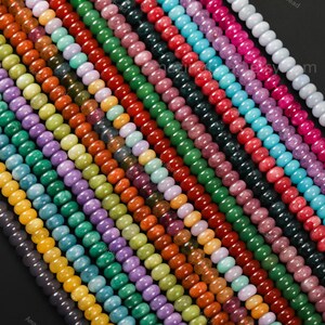 May include: A close-up shot of multiple strands of colorful beads. The beads are in various colors, including green, red, orange, yellow, purple, and blue. The beads are round and appear to be made of stone or glass. The image is well-lit and the colors are vibrant.