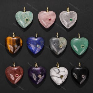 Puede incluir: Una colección de colgantes de piedras preciosas en forma de corazón en varios colores, incluyendo verde, rosa y morado. Cada colgante tiene una fianza dorada y un pequeño acento de piedra preciosa contrastante en el centro.