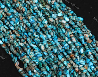Può includere: Un filo di perline di pietre preziose blu turchese e verdi. Le perline sono piccole e di forma irregolare, simili a ciottoli. Le perline sono infilate su un filo trasparente.